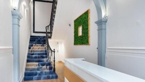Un pasillo con suelo de madera, una escalera con escalones azules y un mostrador de recepción con encimera blanca.
