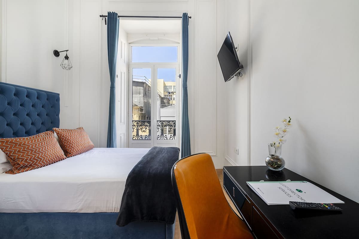 A hotel room with a bed, a desk, a chair, a TV, and a window with curtains.