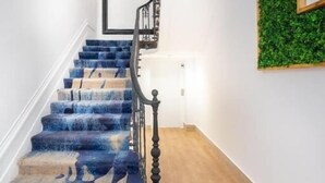 Una escalera con un suelo de madera, un suelo alfombrado con un motivo azul y una decoración verde en la pared.