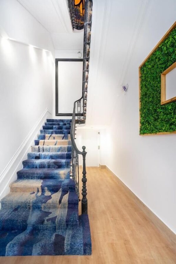 A staircase with a blue patterned carpet, a wooden floor, and a green wall decoration. - Lisbon 5 (Lisbon)
