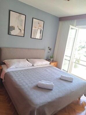 A neatly made bed with a patterned bedspread, two pillows, and folded towels on a wooden floor. - Apartment Carrington (Dubrovnik)