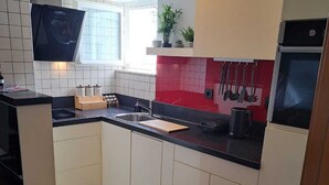 A modern kitchen with a black countertop, white cabinets, and a red backsplash.