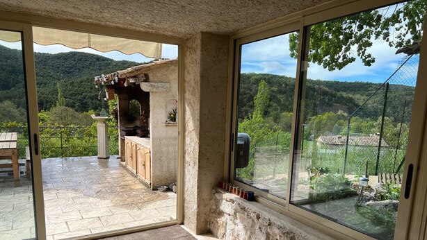 A spacious patio with a stone floor, a wooden bench, and a view of a mountainous landscape through large windows.