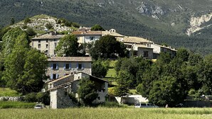 A hillside village with stone buildings, a clear sky, and a mountainous backdrop.