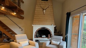 A cozy living room with two grey armchairs, a fireplace, and a wooden ceiling with antlers.