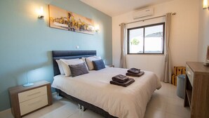 A bedroom with a bed, bedside table, lamp, and artwork on the wall. - 102 Hibiscus Monte Dourado (Carvoeiro)