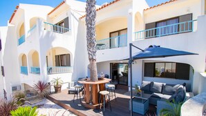 A courtyard with outdoor seating, a palm tree, and a building with balconies. - 102 Hibiscus Monte Dourado (Carvoeiro)