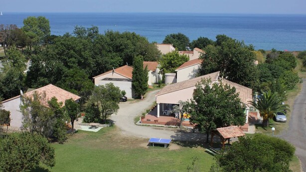 Vista aérea de uma área residencial com casas, uma quadra de tênis e vista para o mar.