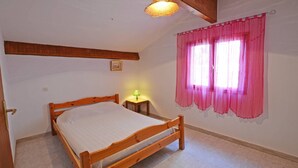 Um quarto com uma cama de madeira, uma mesinha de cabeceira com uma luminária e uma janela com cortinas cor-de-rosa.