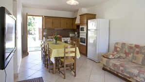 Cozinha compacta com armários de madeira, uma mesa de jantar com cadeiras, geladeira e um sofá.