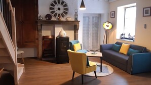 A living room with a wooden staircase, a yellow armchair, a grey sofa, a round coffee table, and a large wall clock. - Gîte Familial « Le Rivallier » Près des Bords de Lallier (Joze)
