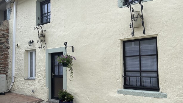 A building with a white exterior, a door with a small window, and a potted plant in front. - Gîte Familial « Le Rivallier » Près des Bords de Lallier (Joze)
