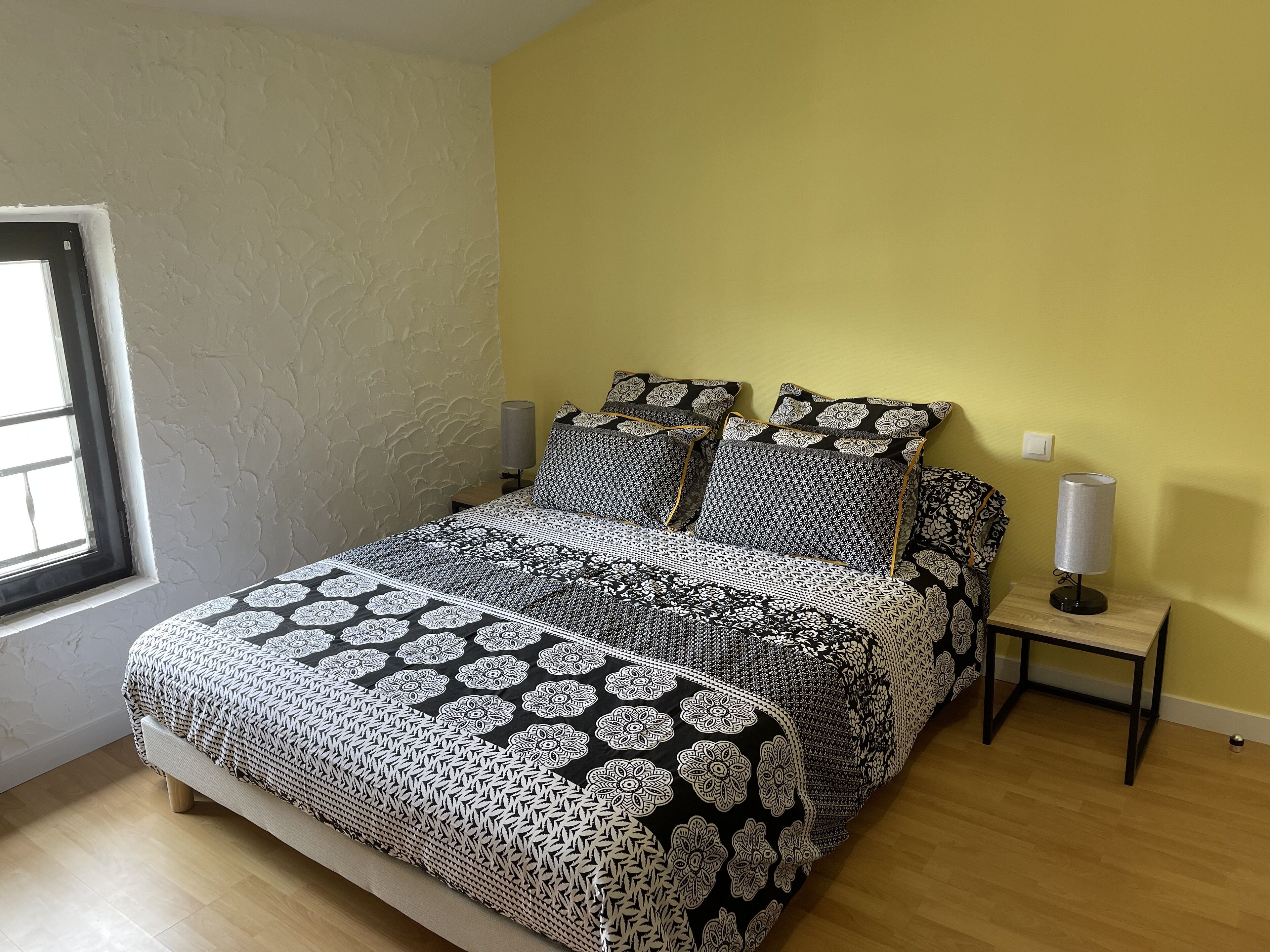 A bedroom with a bed, two bedside tables, a window, and a wall switch.