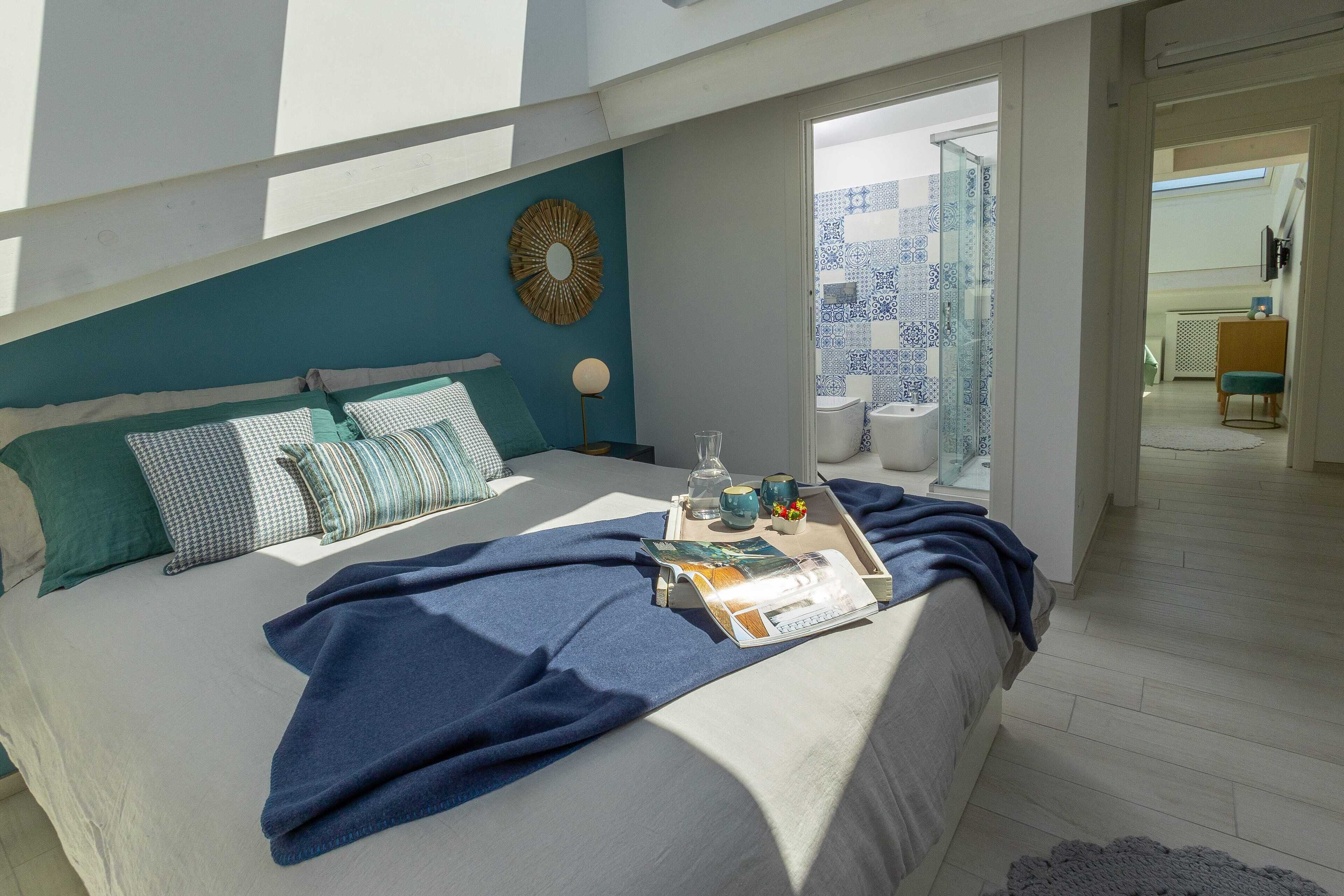 A bedroom with a bed, pillows, a tray with books and glasses, and a view of the bathroom.