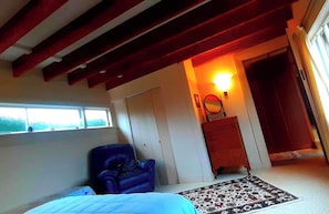 Um quarto com uma cama, uma cadeira azul, cômoda de madeira, tapete e uma janela.
