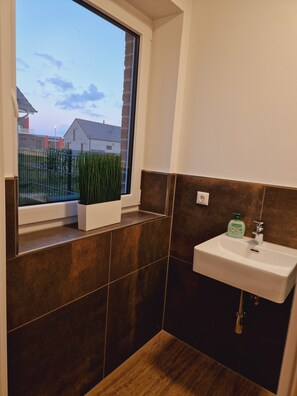 Ein Badezimmer mit Fenster, Waschbecken und einer Topfpflanze.