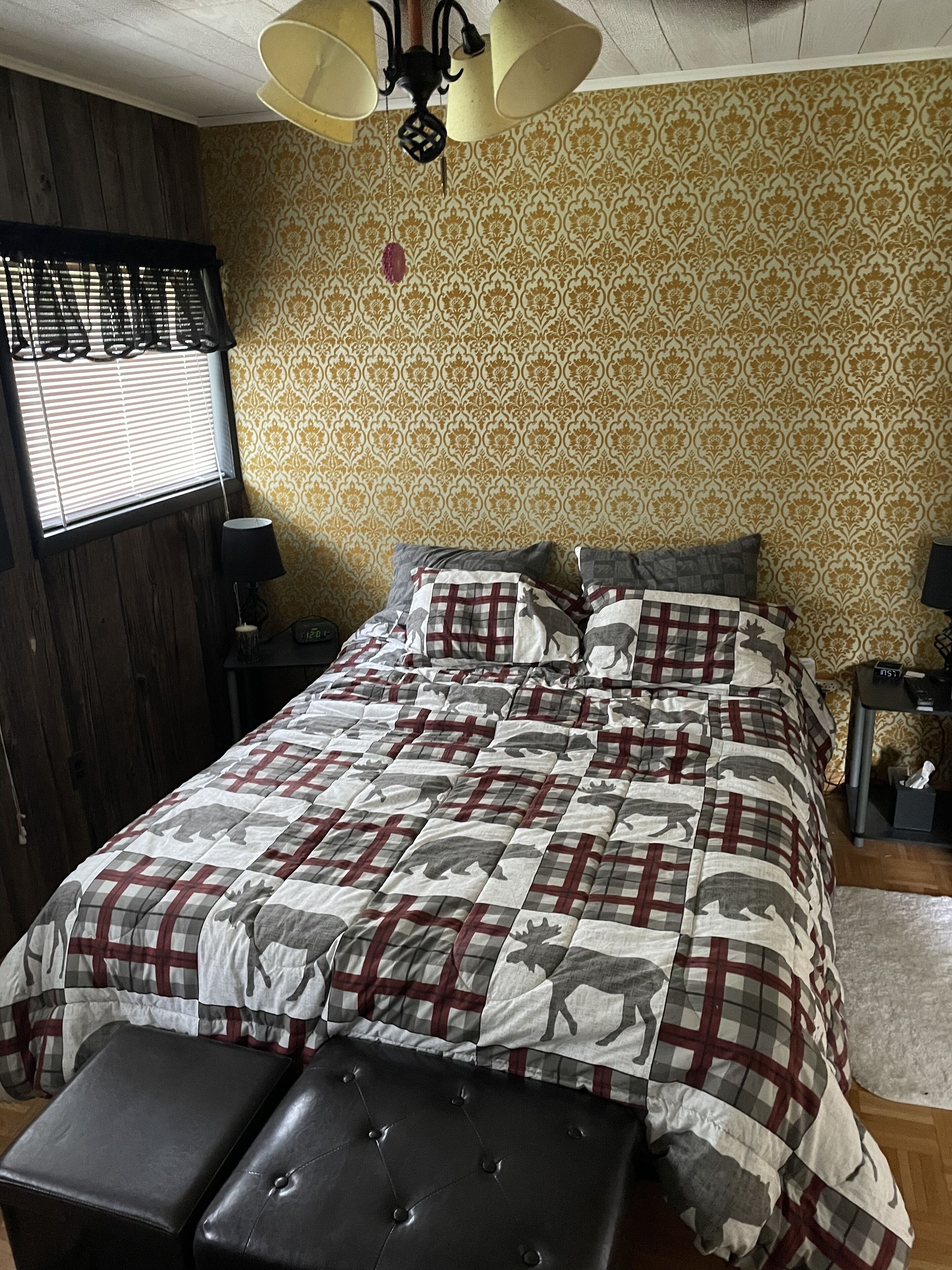 A bedroom with a bed, a bench, a nightstand, a lamp, and a window with blinds.