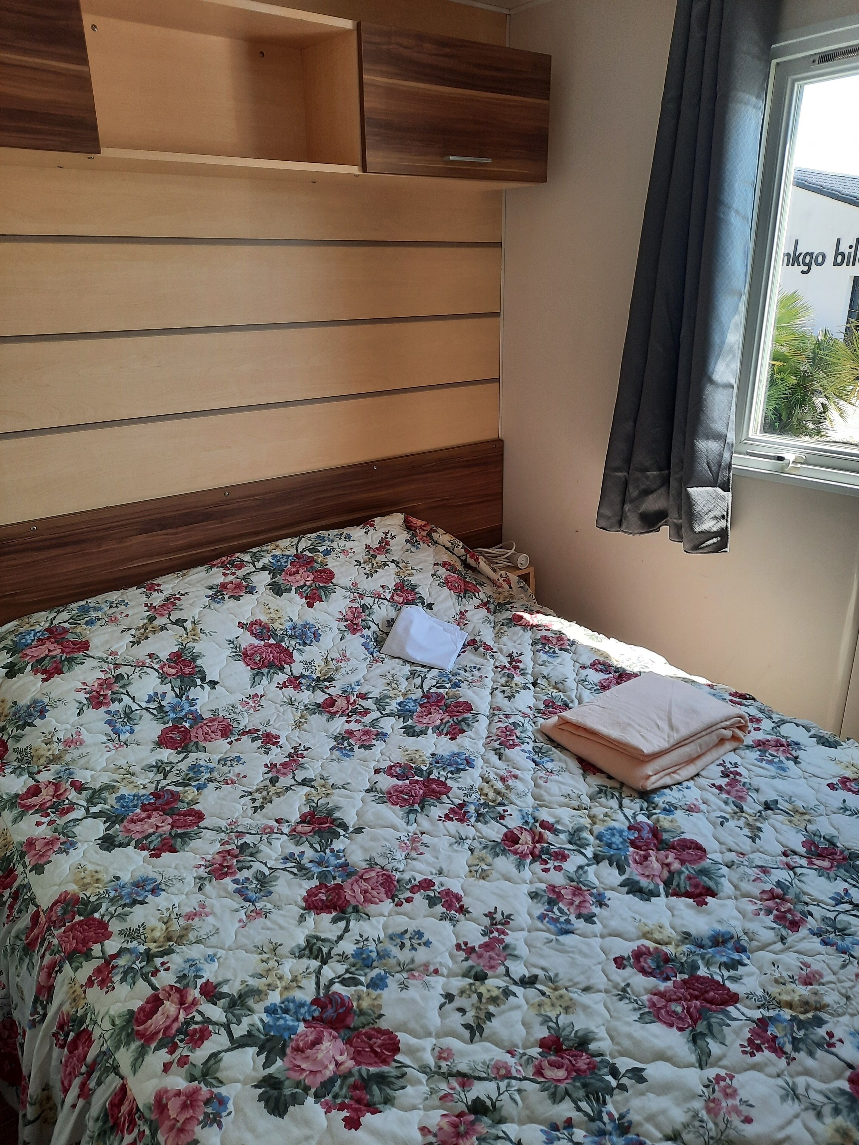 A bed with a floral quilt, a wooden headboard, and a window with curtains.