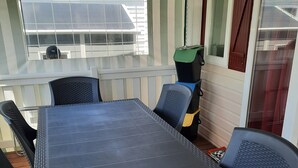 Un'area salotto esterna coperta con tavolo e sedie, una finestra vista e una porta con tenda.