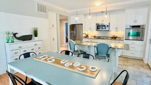 Una cocina moderna con armarios blancos, electrodomésticos de acero inoxidable y un comedor con mesa azul claro y sillas negras.