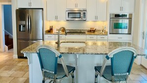 Una cocina moderna con gabinetes blancos, electrodomésticos de acero inoxidable, una encimera de granito y dos sillas azules.