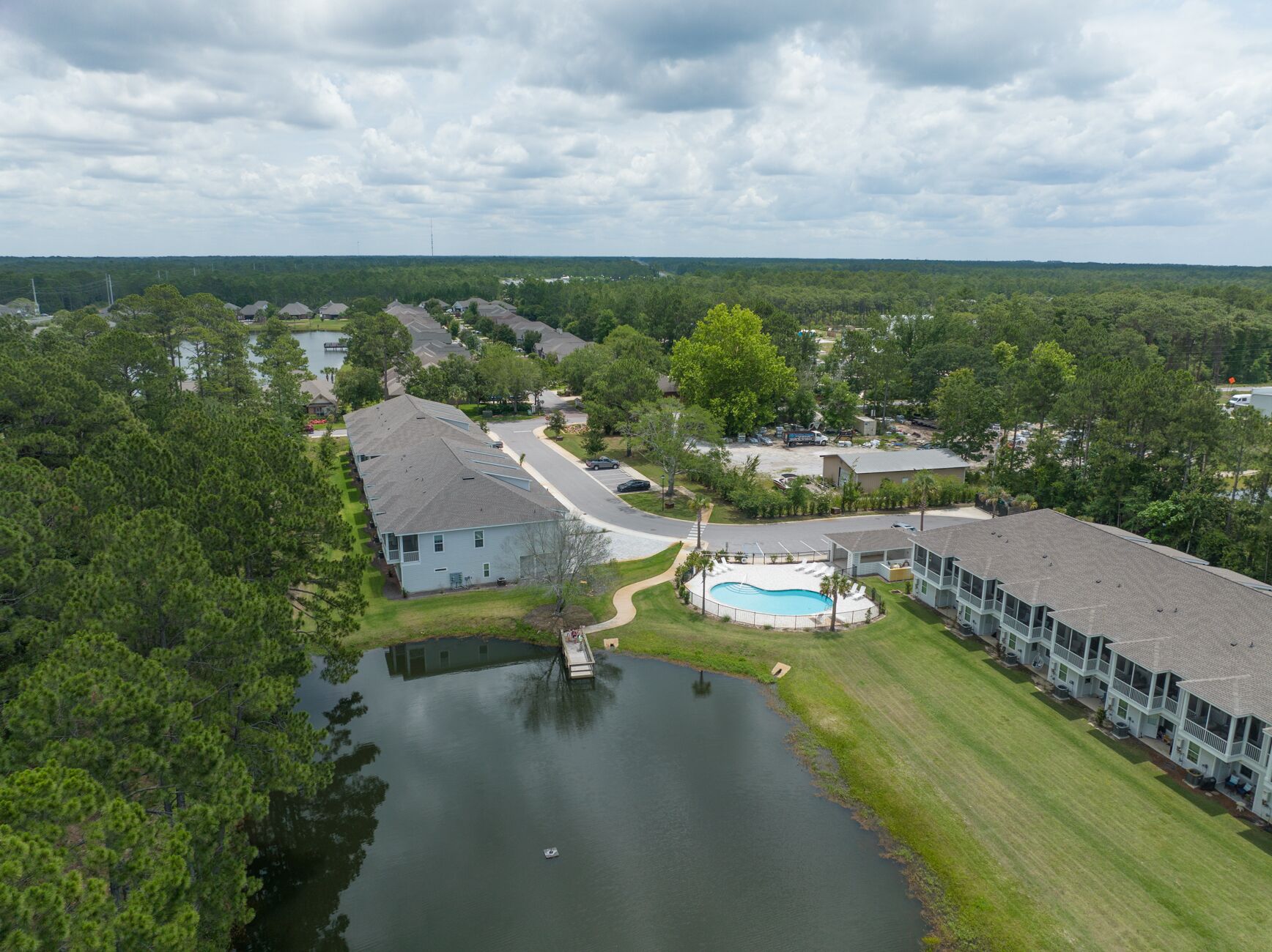A residential area with a swimming pool, houses, and a large body of water.