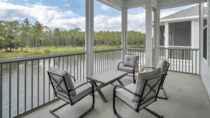 A covered balcony with a table and chairs, overlooking a lake and forest. - BRAND NEW Santa Rosa Beach/30A 4 Bedroom 3 Bathroom (Santa Rosa Beach)