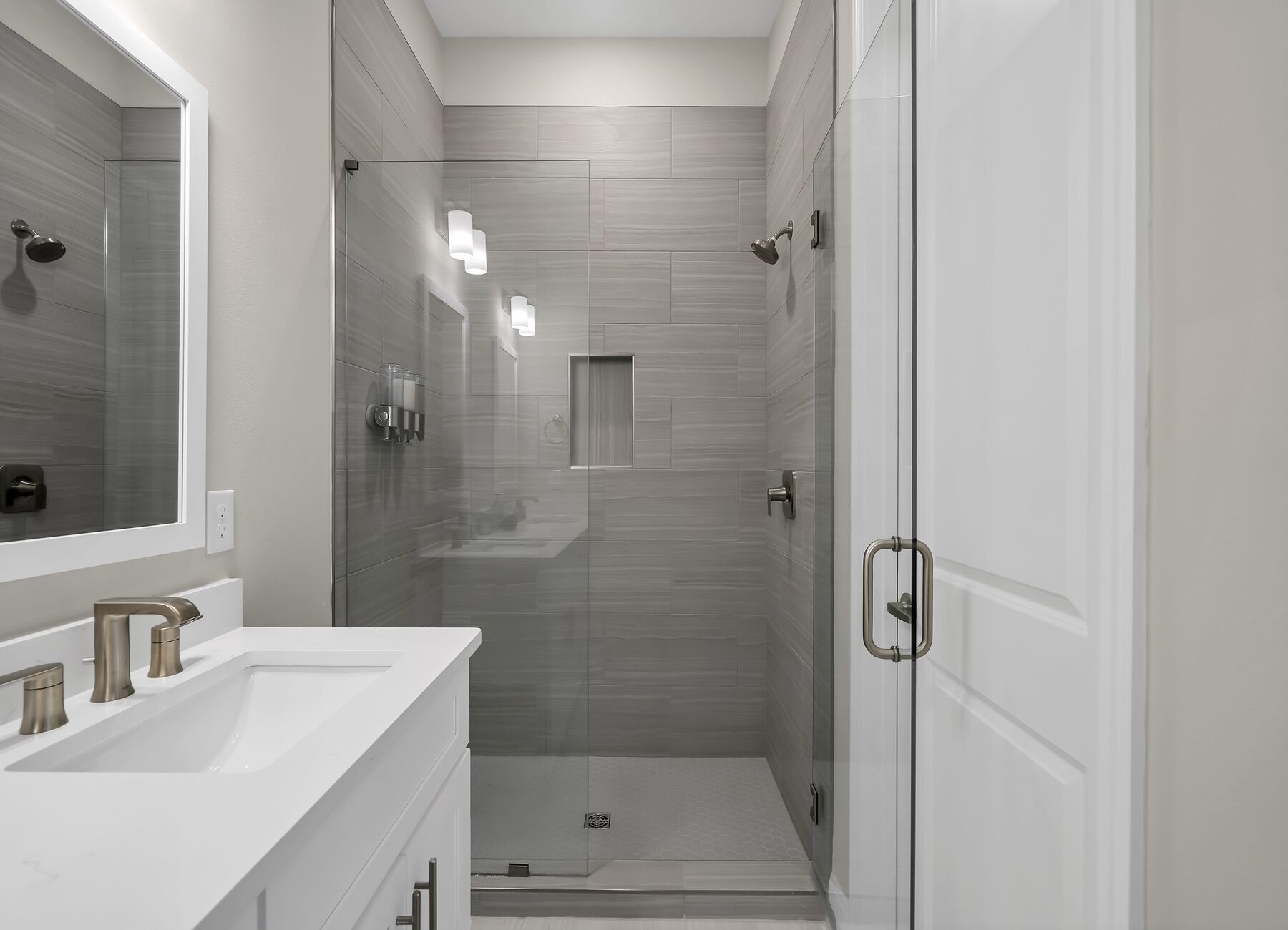 A modern bathroom with a glass shower enclosure, a white sink with a single faucet, and a door with a handle.