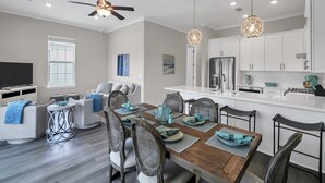 A modern kitchen with white cabinets, a stainless steel refrigerator, and a dining area with a wooden table and chairs. - BRAND NEW Santa Rosa Beach/30A 4 Bedroom 3 Bathroom (Santa Rosa Beach)