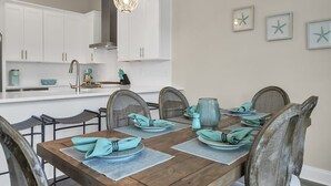 A dining area with a wooden table set for six, surrounded by wicker chairs. - BRAND NEW Santa Rosa Beach/30A 4 Bedroom 3 Bathroom (Santa Rosa Beach)