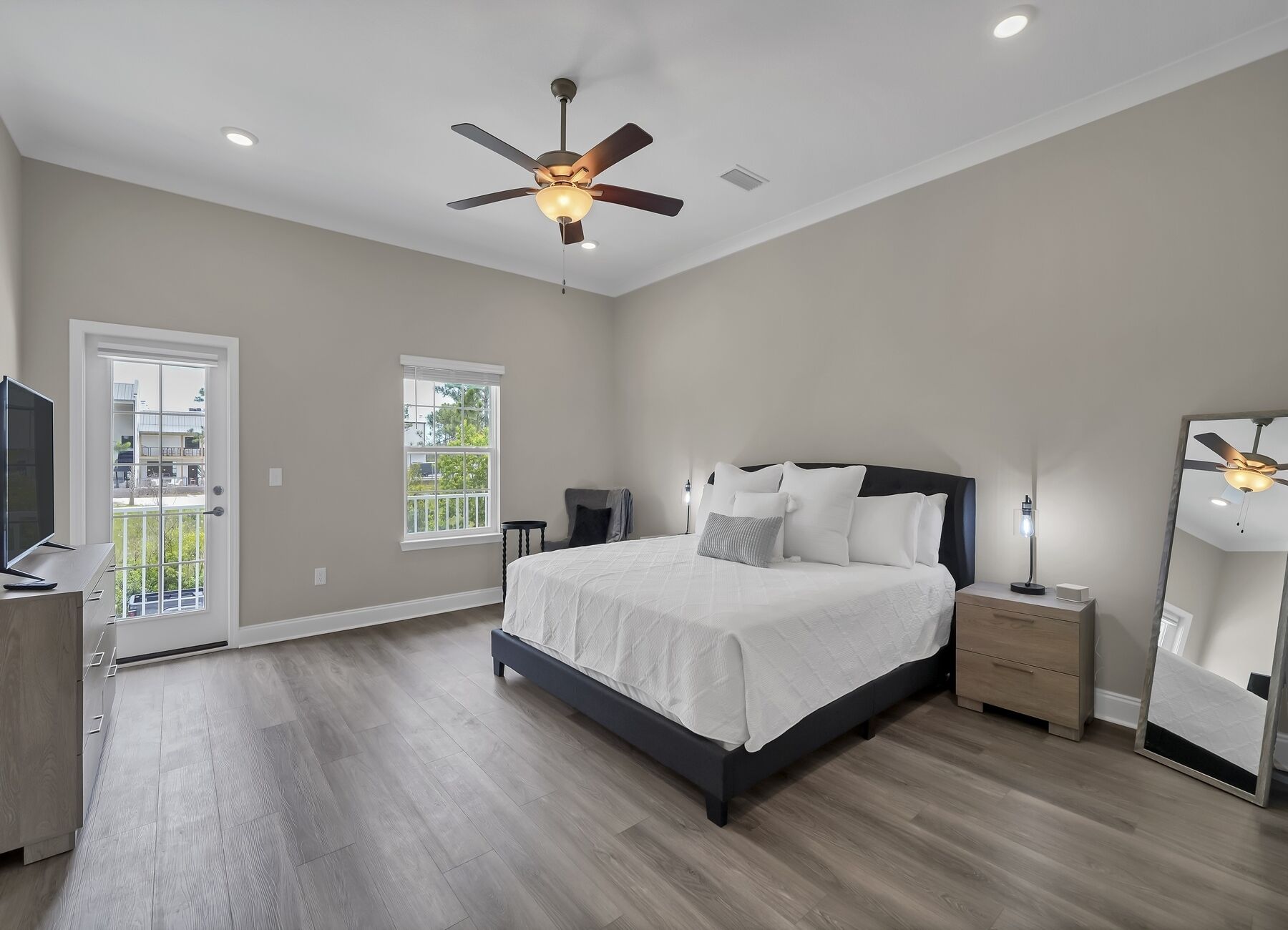 A bedroom with a bed, a ceiling fan, a nightstand, a lamp, a TV, and a window with a view of the outside.