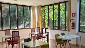 A dining area with tables and chairs, large windows with curtains, and a fire extinguisher on the wall. - CiaoMi - Hostel & Long Stay - Milano Niguarda & Bicocca  (Milan)