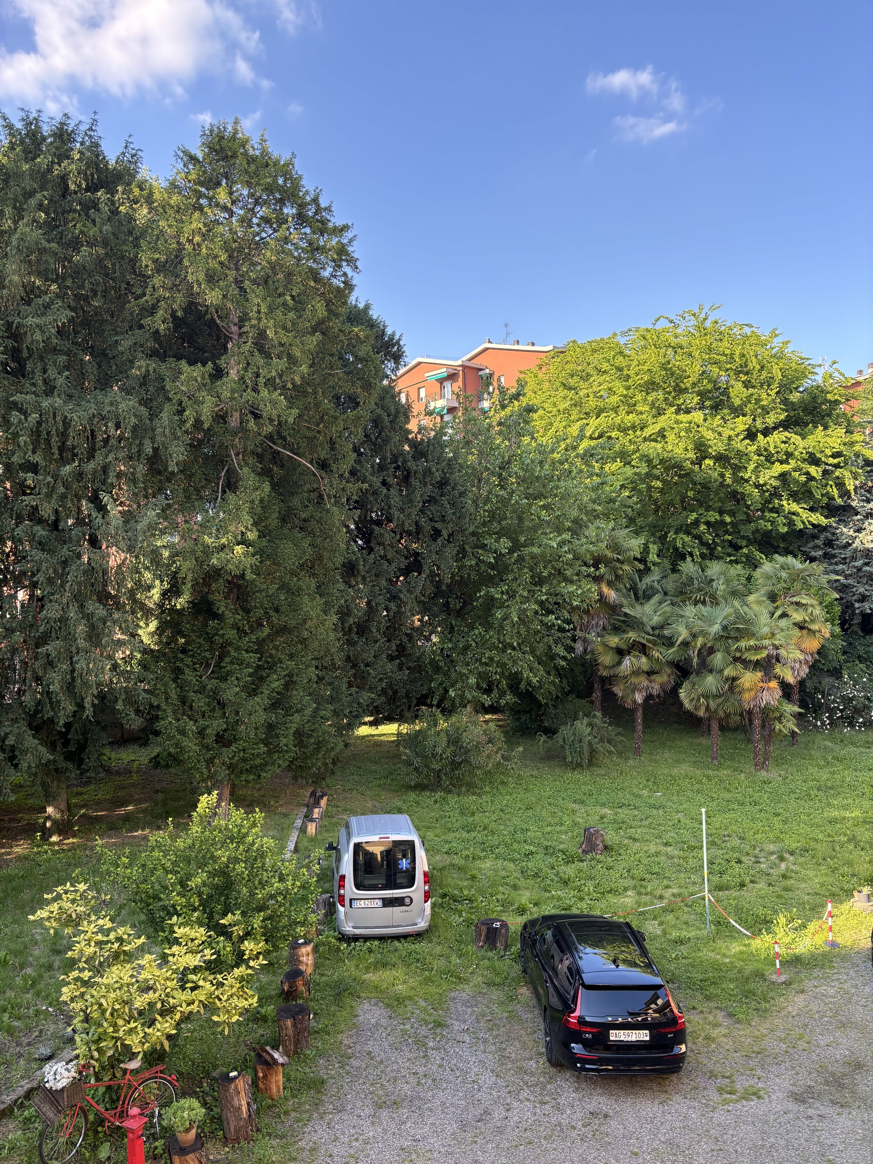 Ein Kiesweg mit einem weißen Lieferwagen und einem schwarzen Auto, umgeben von üppigem Grün und Bäumen.