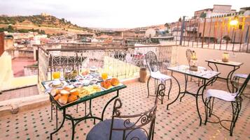A rooftop terrace with a table set for breakfast, chairs, and a view of the cityscape.