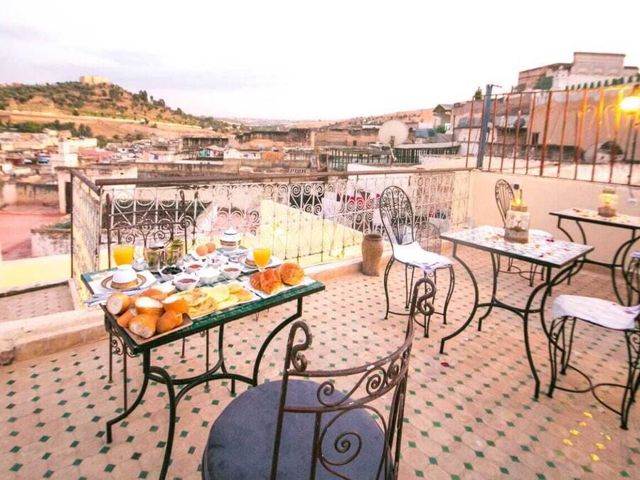 A rooftop terrace with a table set for breakfast, chairs, and a view of the cityscape.