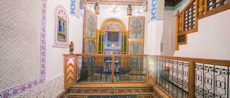 A traditional interior with ornate tile work, a balcony with a wrought iron railing, and a chandelier.