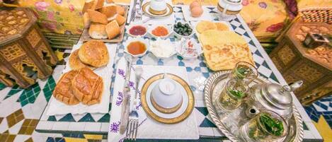 A traditional Moroccan dining setup with a variety of breads, pastries, and condiments on a patterned tablecloth.