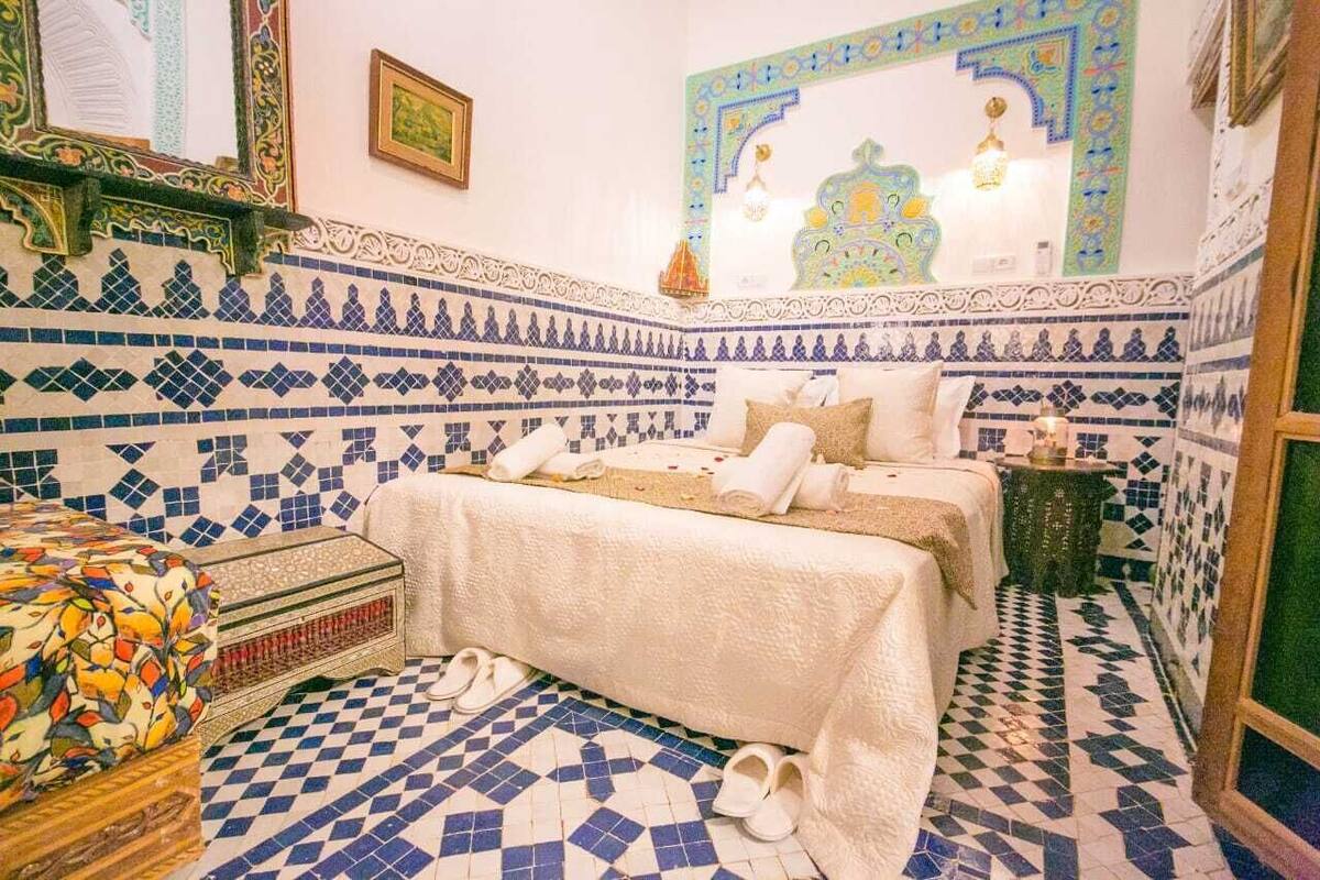 A room with a bed, a small table, and a colorful sofa.