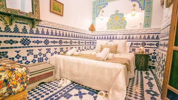 A room with a bed, a small table, and a colorful sofa.