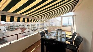 Uma sala de jantar com uma mesa posta para quatro pessoas, com vista para uma área residencial com varandas.