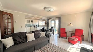 Uma sala de estar moderna com um sofá cinzento, poltronas vermelhas e uma área de jantar com mesa e cadeiras.