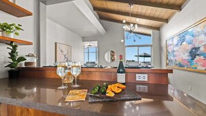 A modern kitchen with a wooden countertop, wine glasses, a bottle of wine, and a cutting board with fruit.