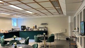 A spacious room with a high ceiling, a kitchen area, and several round tables with green upholstered chairs. - HOTELL CITY KARLSHAMN (Karlshamn)