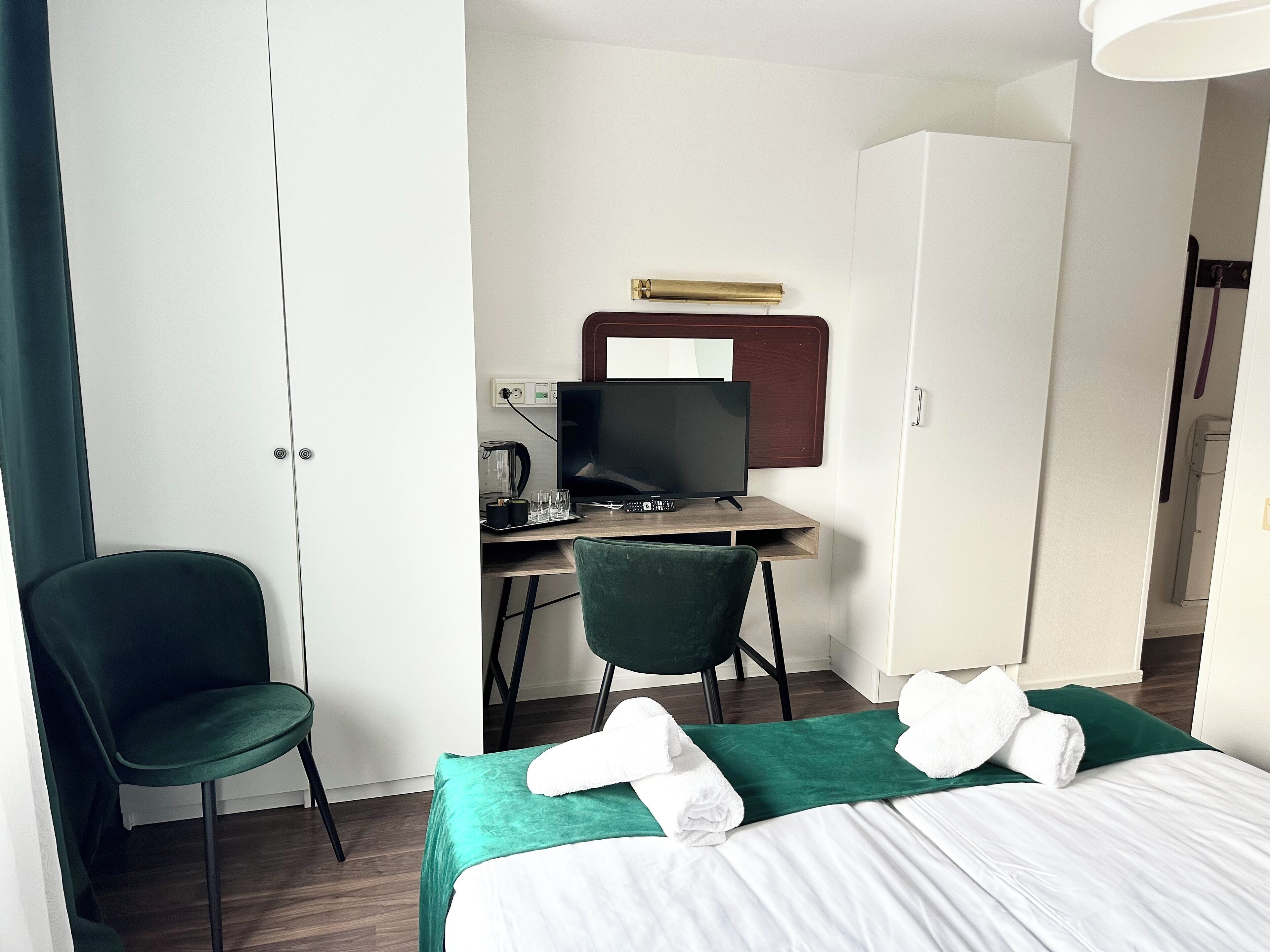 Una habitación de hotel con cama, escritorio con computadora, una silla y un armario.