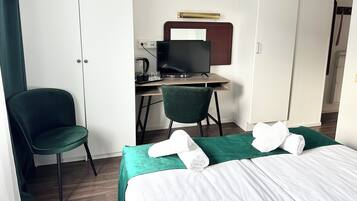 Una habitación de hotel con cama, escritorio con computadora, una silla y un armario.