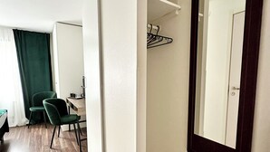 A hotel room with a wooden floor, a desk with a chair, a mirror, and a coat rack. - HOTELL CITY KARLSHAMN (Karlshamn)