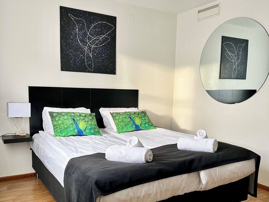 Ein ordentlich bezogenes Bett mit zwei grün-blauen Kissen, einem schwarzen Kopfteil und einer weißen Nachttischlampe.