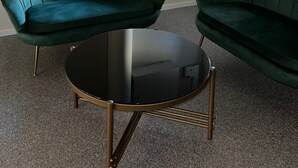 A room with two green upholstered sofas, a round black table with gold legs, a white radiator, and a window with blinds. - HOTELL CITY KARLSHAMN (Karlshamn)