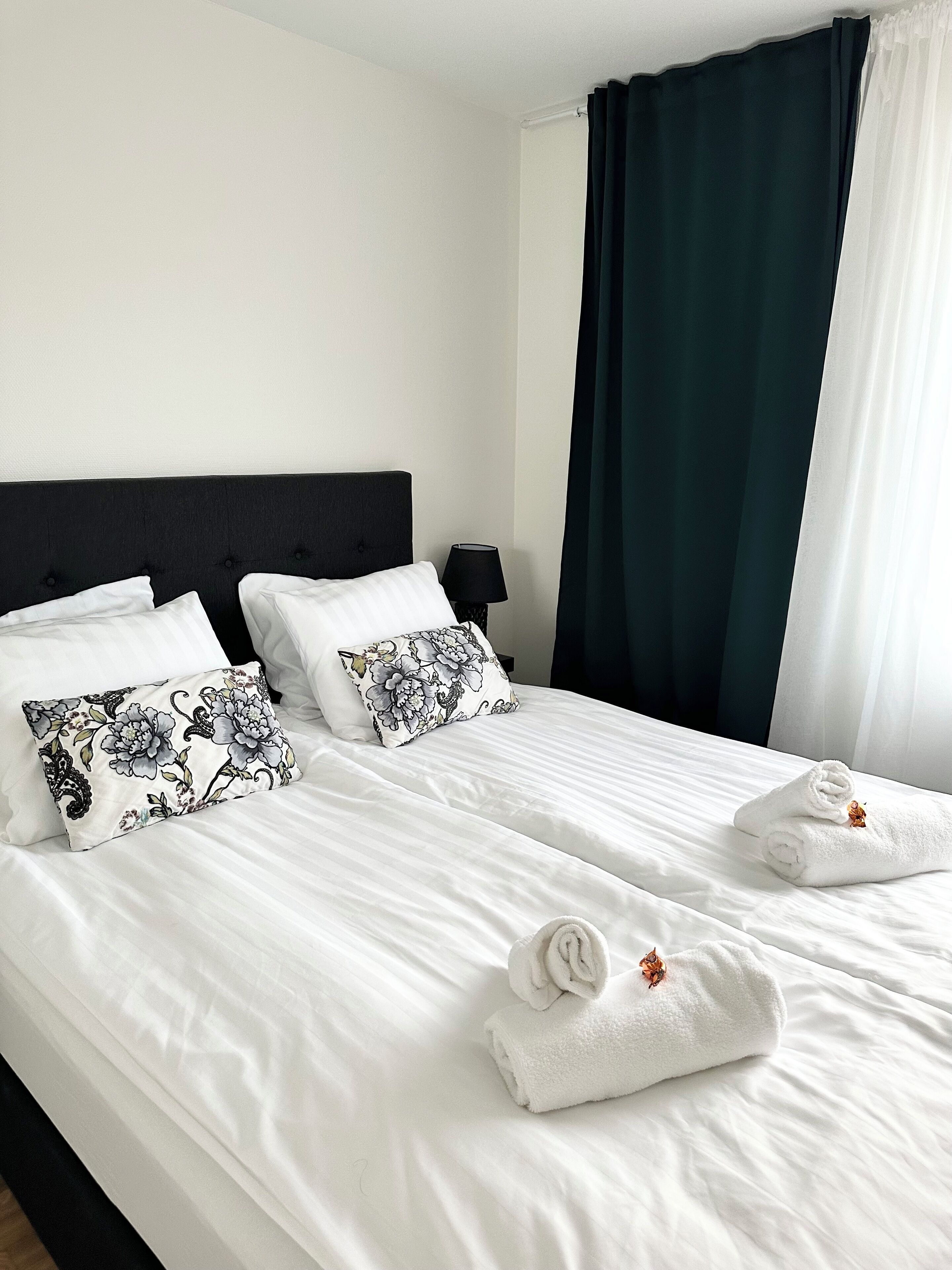 A neatly made bed with white linens, two decorative pillows, and two folded towels.