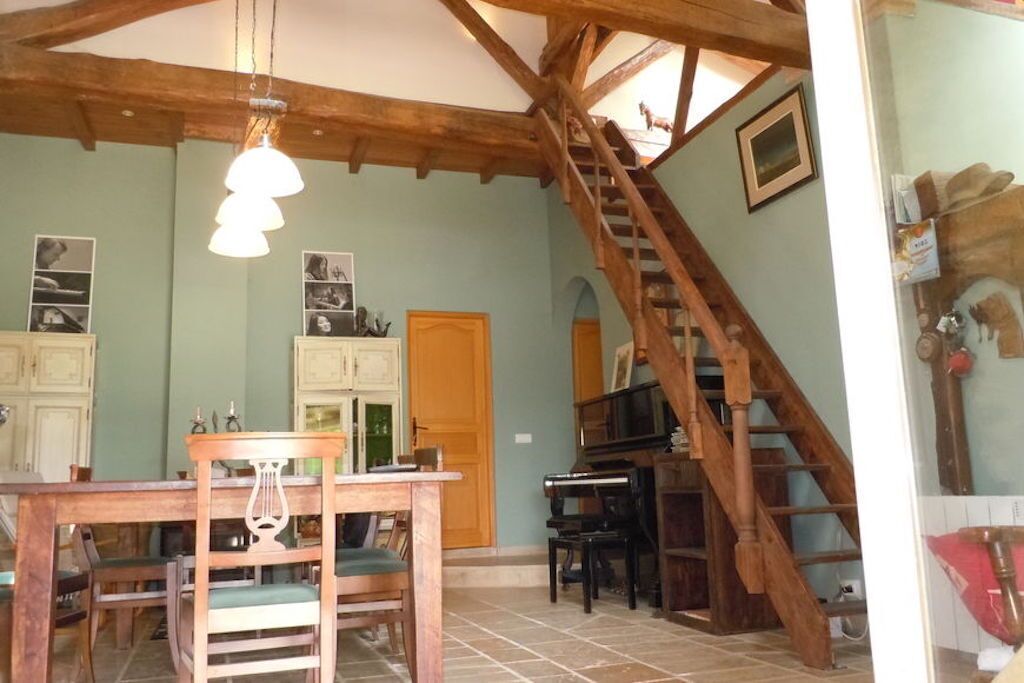 A dining area with a wooden table and chairs, a piano, and a staircase leading to an upper level.